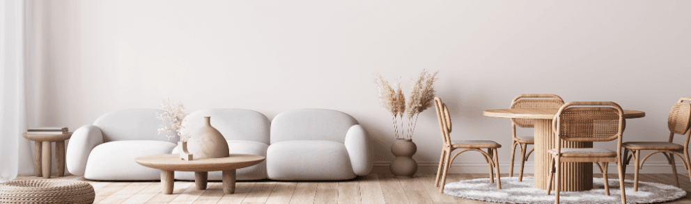 Wohnzimmer mit beiger Wand, einer Essgruppe aus Holz und einem Sofa in hellgrau vor dem ein Holztisch mit Deko steht